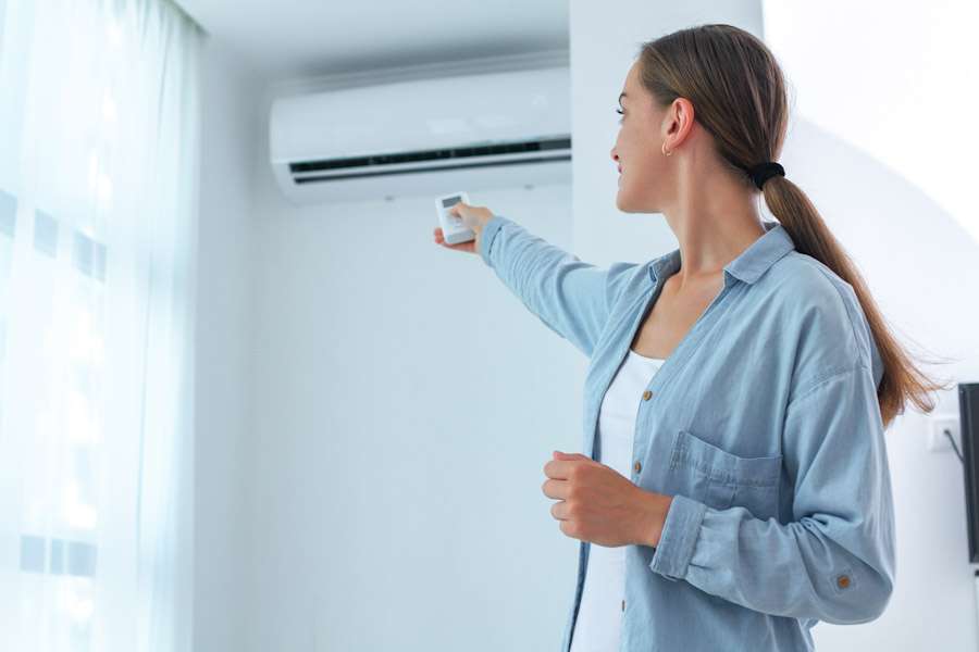 dorscht-waermepumpe-coburg-erdwaerme Person bedient mit einer Fernbedienung eine moderne Split-Klimaanlage an der Wand in einem hellen Wohnraum.